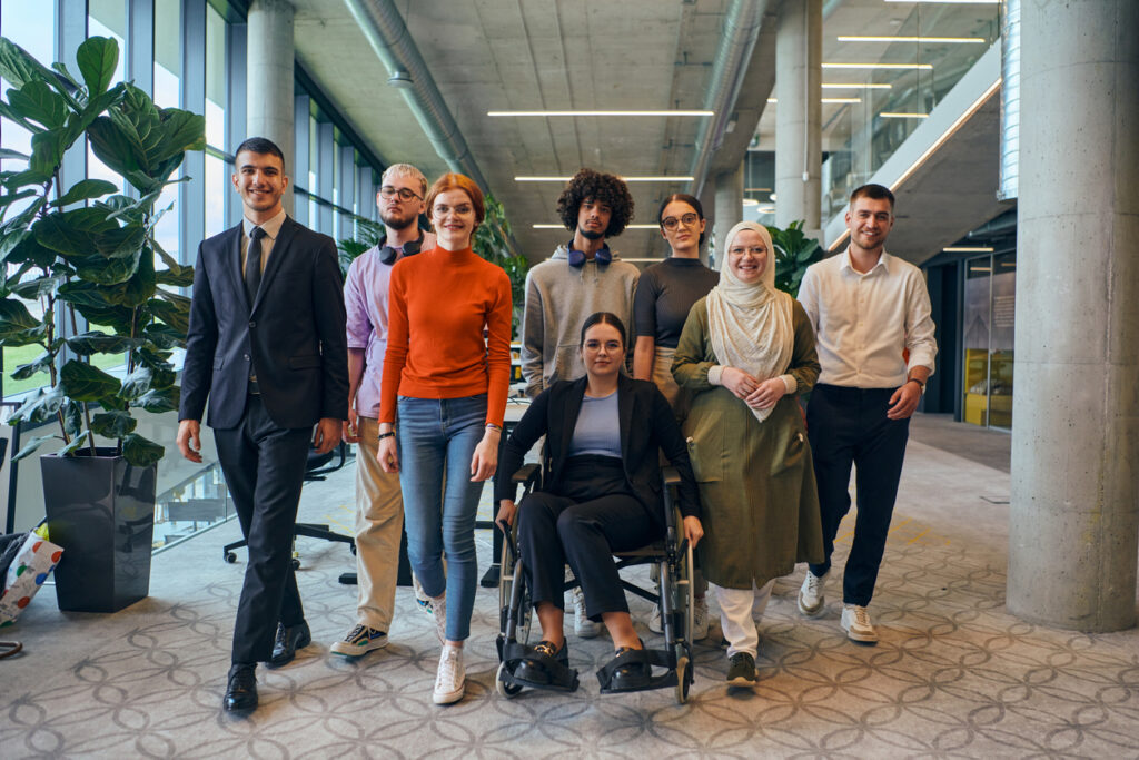 In a spacious and modern startup office, a diverse group of business colleagues, including a colleague in a wheelchair, collaborates and interacts, exemplifying inclusivity, diversity, and teamwork in the contemporary corporate world.